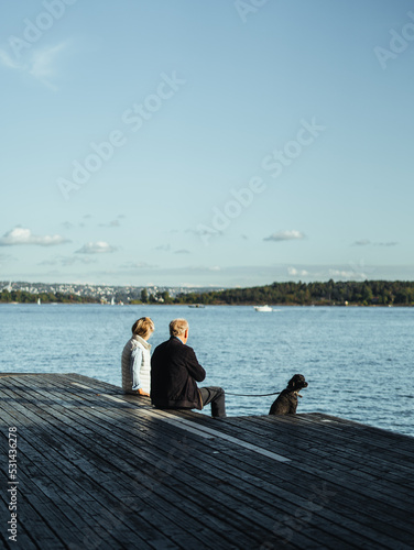 Älteres Ehepaar mit Hund sitzt am Wasser und schaut in die ferne
