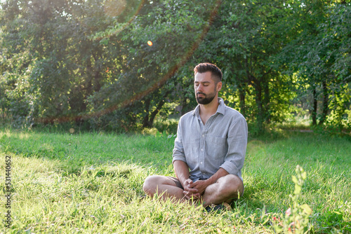 Portrait of young handsome European man in casual clothing sitting on a grass in summer park.