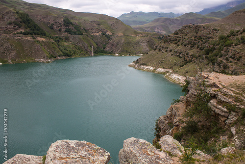 Mountain lake Gizhgit with beautiful turquoise water and high hilly shores on a cloudy summer day and a space for copying in the Elbrus region in the North Caucasus