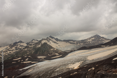 Panoramic landscape - pointed peaks of mountains with white snow and glaciers on the slopes and cloudy sky with dramatic clouds with a blurred horizon in the Elbrus region in the northern Caucasus