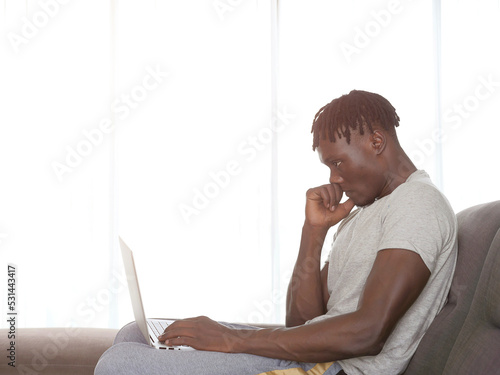 African man sit on couch using laptop, side view, working from home.