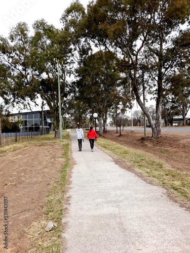 La gente que camina por el sendero peatonal del parque de la ciudad, la madre y la hija que hacen ejercicios diarios para la salud, forman un diseño natural original con el fondo de la arboleda