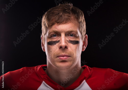 Male American football players looks confidently into the camera without helmet and with under eye make-up.
