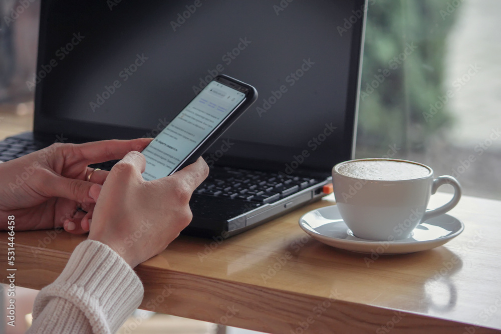 Side image of beautiful woman in striped shirt calling by smartphone while touching a white blank screen computer tablet with keyboard case and sitting at the wooden table with windows as background. Side image of beautiful woman in striped shirt calling by smartphone while touching a white blank screen computer tablet with keyboard case and sitting at the wooden table with windows as background.