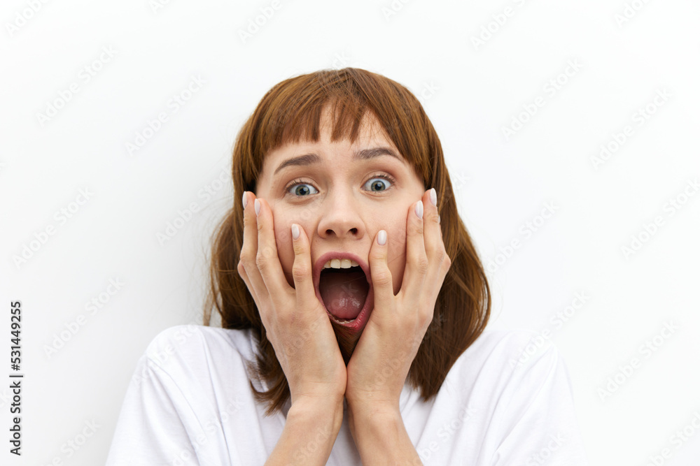 a close horizontal studio photo of a red-haired woman screaming loudly clutching her head from shock. a close horizontal studio photo of a red-haired woman screaming loudly clutching her head from shock.
