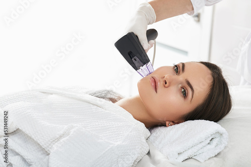 Woman while RF lifting procedure for her face skin tightening with cosmetologist at a beauty salon