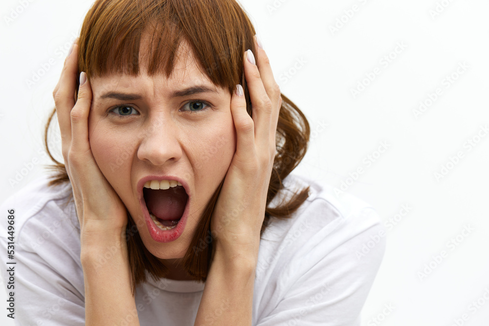a close horizontal studio photograph of an alarmed, frightened woman with red hair, screaming loudly clutching her head from shock. a close horizontal studio photograph of an alarmed, frightened woman with red hair, screaming loudly clutching her head from shock.