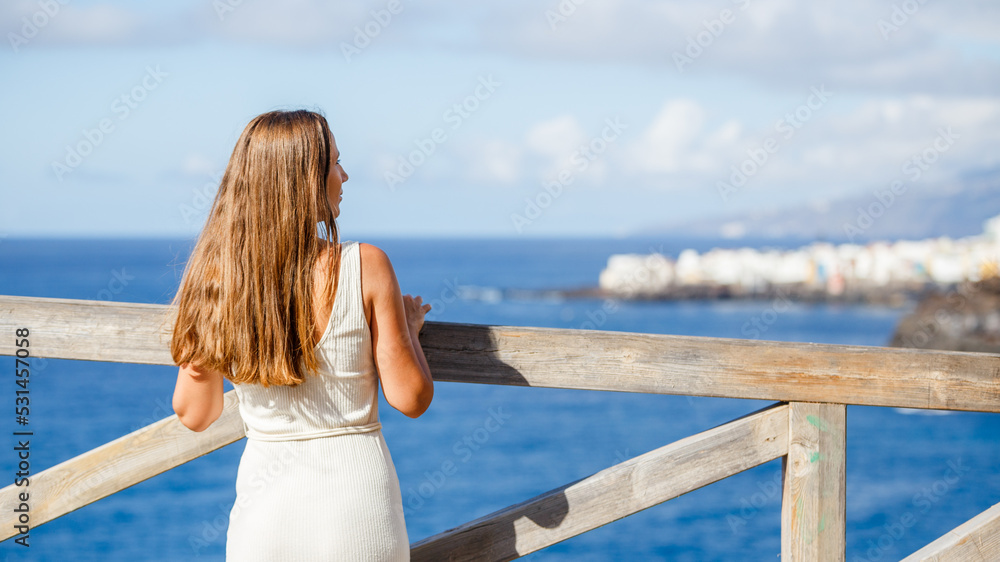 Young woman standing at viewpoint near the sea and looking at the city at horizon
