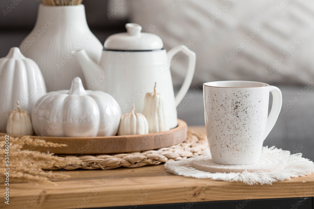 Still-life. Dried pampas grass in a vase, white ceramic pumpkins, a teapot, a cup and pumpkin-shaped candles on a coffee table in the home interior of the living room. Cozy autumn concept. Still-life. Dried pampas grass in a vase, white ceramic pumpkins, a teapot, a cup and pumpkin-shaped candles on a coffee table in the home interior of the living room. Cozy autumn concept.