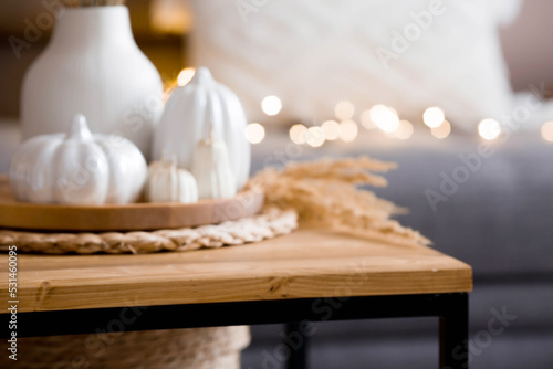 Still-life. White ceramic pumpkins, pampas grass, pumpkin-shaped candles on the coffee table in the home interior of the living room. Details of the decor. Cozy autumn concept.