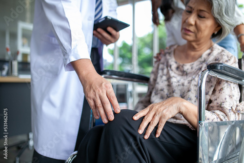 Asian doctor checking knee of elderly patient on wheelchair, healthcare and medical concept.