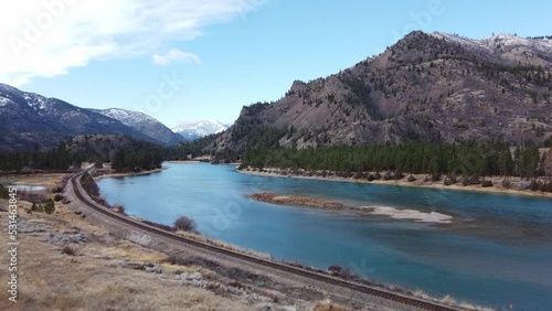 Shot alongside calm and wide river in rural Montana over train tracks on a beautiful day with mountain range in the background