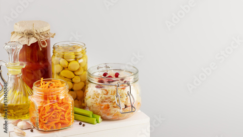 Autumn seasonal pickled or fermented vegetables, mushrooms and olive oil in glass jars on a white wooden board on a light neutral background with copy space. Fall home food preserving or canning