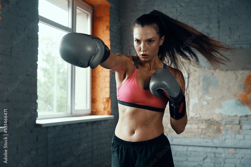 Beautiful young woman practicing her punch while standing in gym - obrazy, fototapety, plakaty 