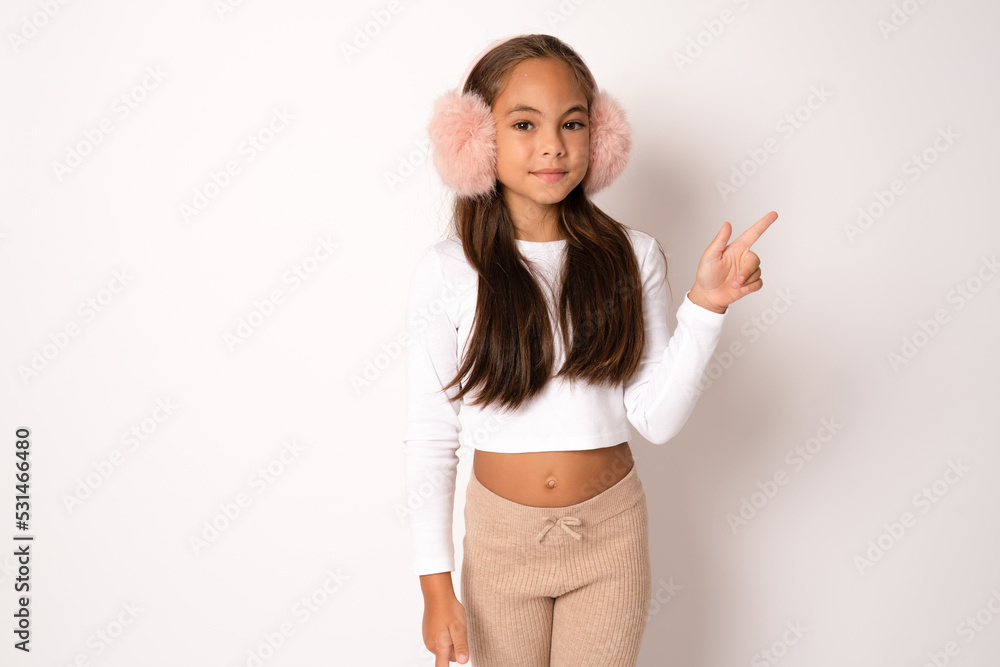 © Danko - Full length portrait of brunette hispanic girl in earmuffs showing and pointing up with fingers number one while smiling confident and happy. © Danko - Full length portrait of brunette hispanic girl in earmuffs showing and pointing up with fingers number one while smiling confident and happy.