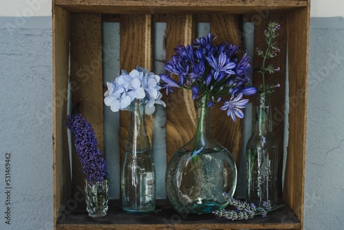 Canvas Print Beautiful shot of assorted colorful flowers in individual vases on a wooden shel