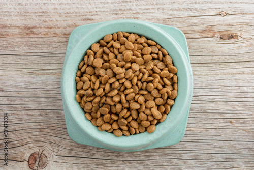 Dry food for cats and dogs in a green bowl on a wooden background.