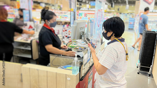 Asian woman wearing a mask while using mobile phone to make contactless payments at supermarket cashier position. photo