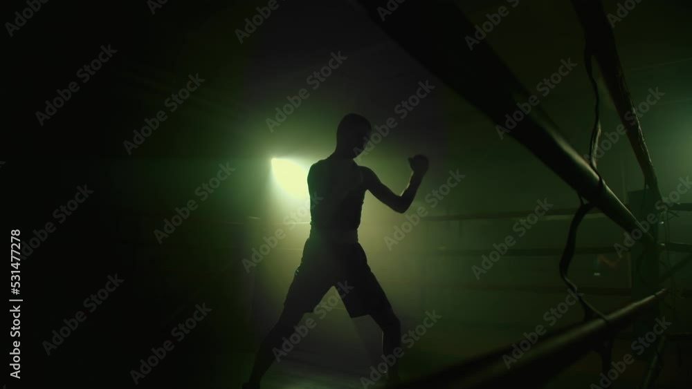 Lightweight fighter training inside the boxing ring. Silhouette of a boxer or kickboxer athlete punching the air, shadow fight in a empty foggy gym Lightweight fighter training inside the boxing ring. Silhouette of a boxer or kickboxer athlete punching the air, shadow fight in a empty foggy gym