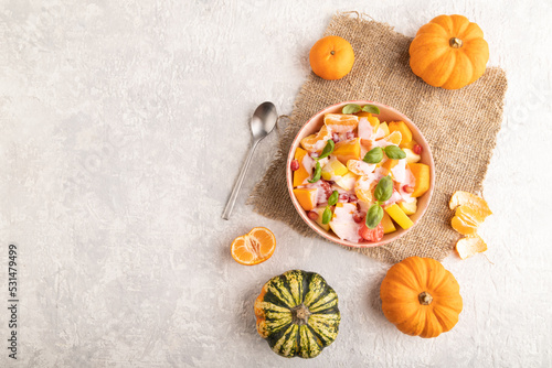 Vegetarian fruit salad of yogurt pumpkin, tangerine, basil microgreen on gray, top view, copy space.