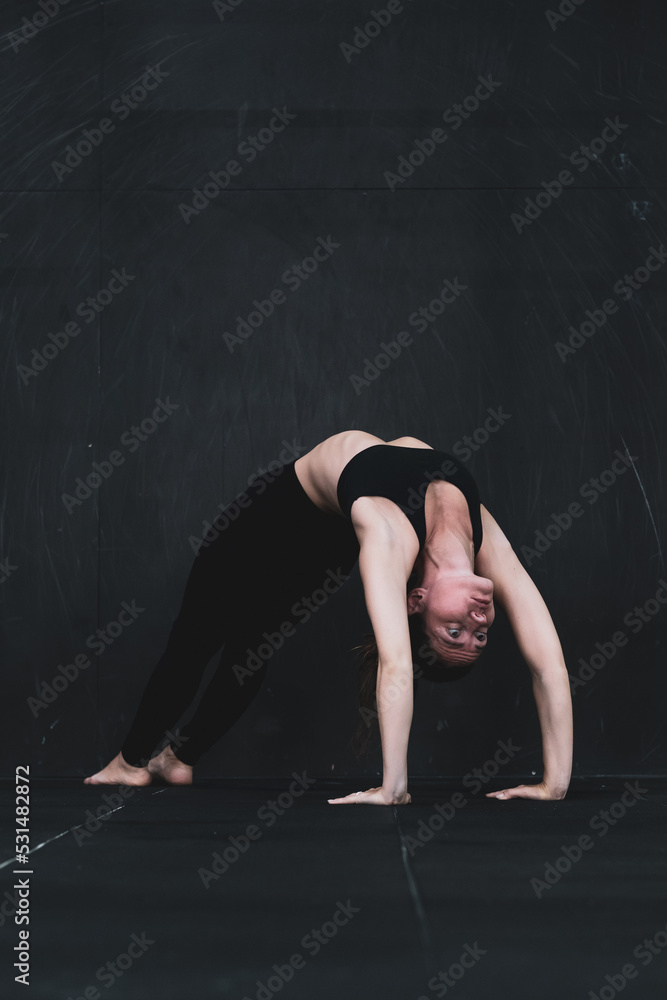 Young woman meditates, doing yoga poses and asana. Fitness girl enjoying yoga indoors. A yoga gymnast girl on a dark background. Black on Black	
