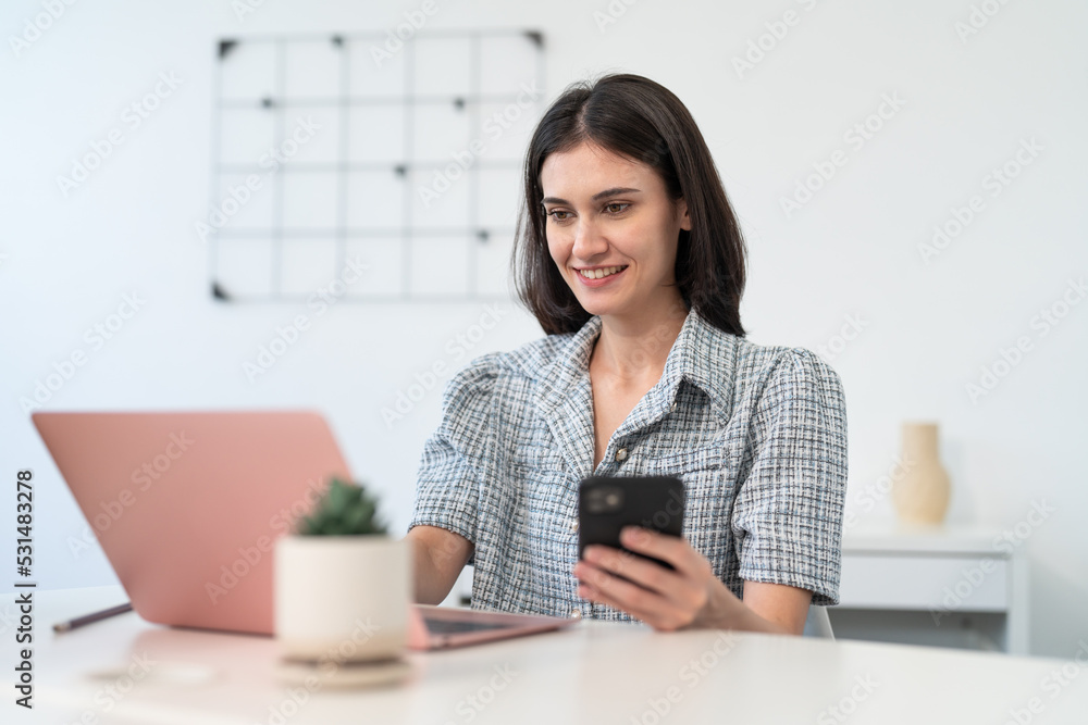 Smiling beautiful woman using laptop and smartphone while working at office Smiling beautiful woman using laptop and smartphone while working at office