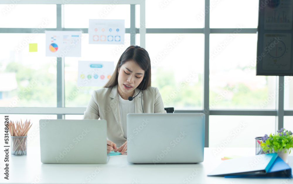 Young asian woman working at a call center Consulting about stock investment information with customers calling for advice with emotion of serious Young asian woman working at a call center Consulting about stock investment information with customers calling for advice with emotion of serious