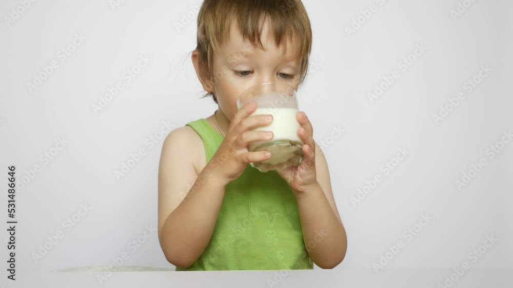 A cute little boy drinks some milk from a glass against white background A cute little boy drinks some milk from a glass against white background