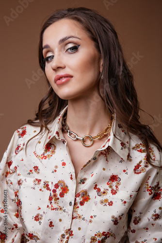 High fashion photo of a beautiful elegant young woman in a pretty patterned shirt, white short skirt, tights, brown shoes, accessories posing over beige background. Studio Shot. Portrait. 