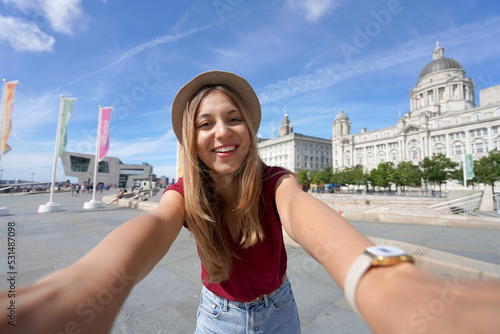 Tourism in Liverpool, UK. Beautiful young woman takes selfie picture in front of Pier Head with 