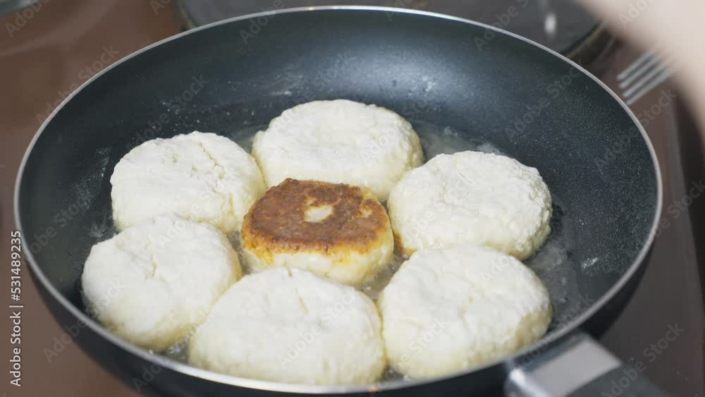 Many cheesecakes are fried in a frying pan on an electric stove. Breakfast preparation. Many cheesecakes are fried in a frying pan on an electric stove. Breakfast preparation.