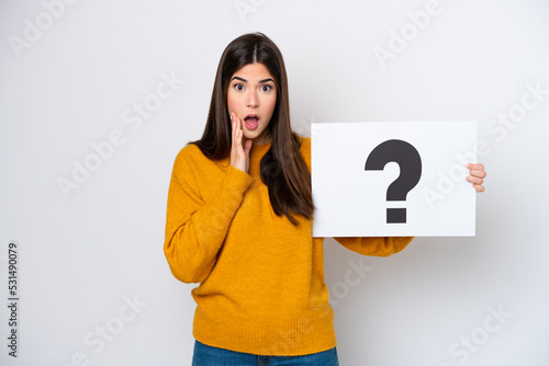 Young Brazilian woman isolated on white background holding a placard with question mark symbol with surprised expression