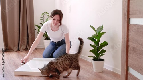 Woman unpacks a new white coffee table on floor and the cat walks nearby