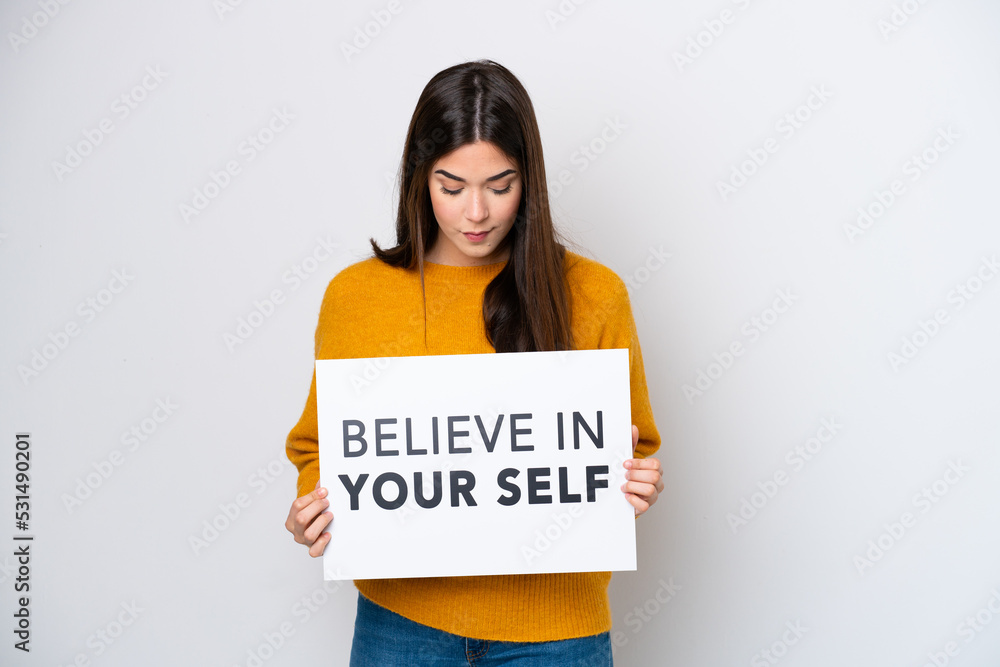 Young Brazilian woman isolated on white background holding a placard with text Believe In Your Self Young Brazilian woman isolated on white background holding a placard with text Believe In Your Self