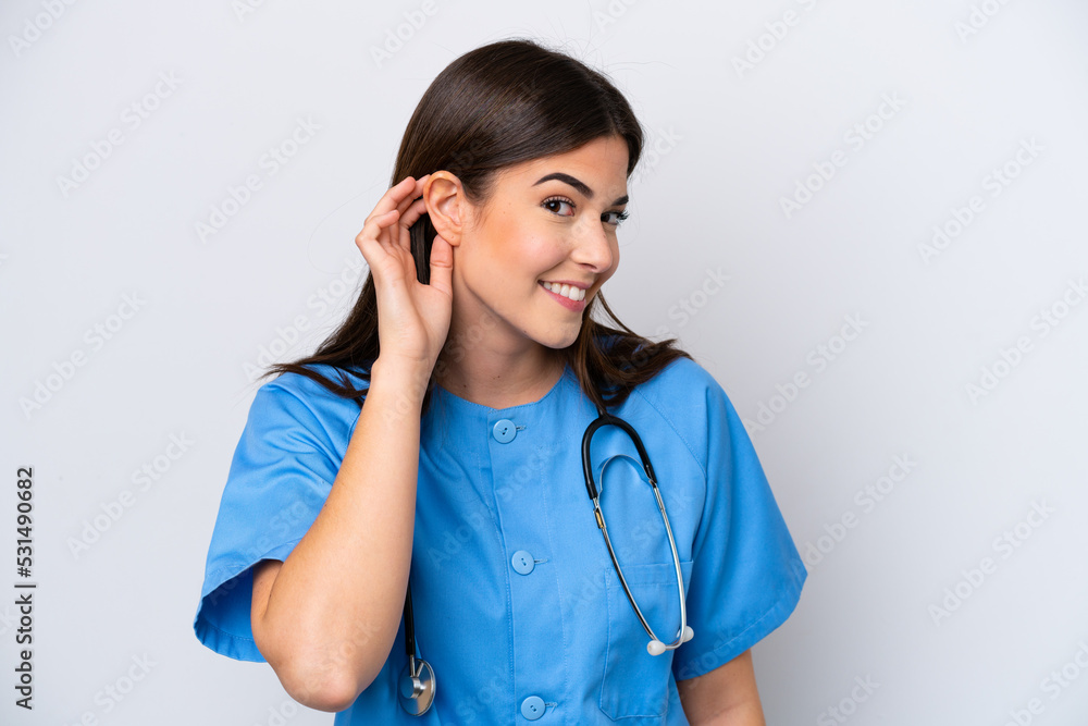 Young Brazilian nurse woman isolated on white background listening to something by putting hand on the ear Young Brazilian nurse woman isolated on white background listening to something by putting hand on the ear