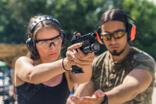 handsome male instructor in moro T-shirt helping a Caucasian girl to hold a pistol with a torch and collimator correctly, medium closeup shooting range. High quality photo