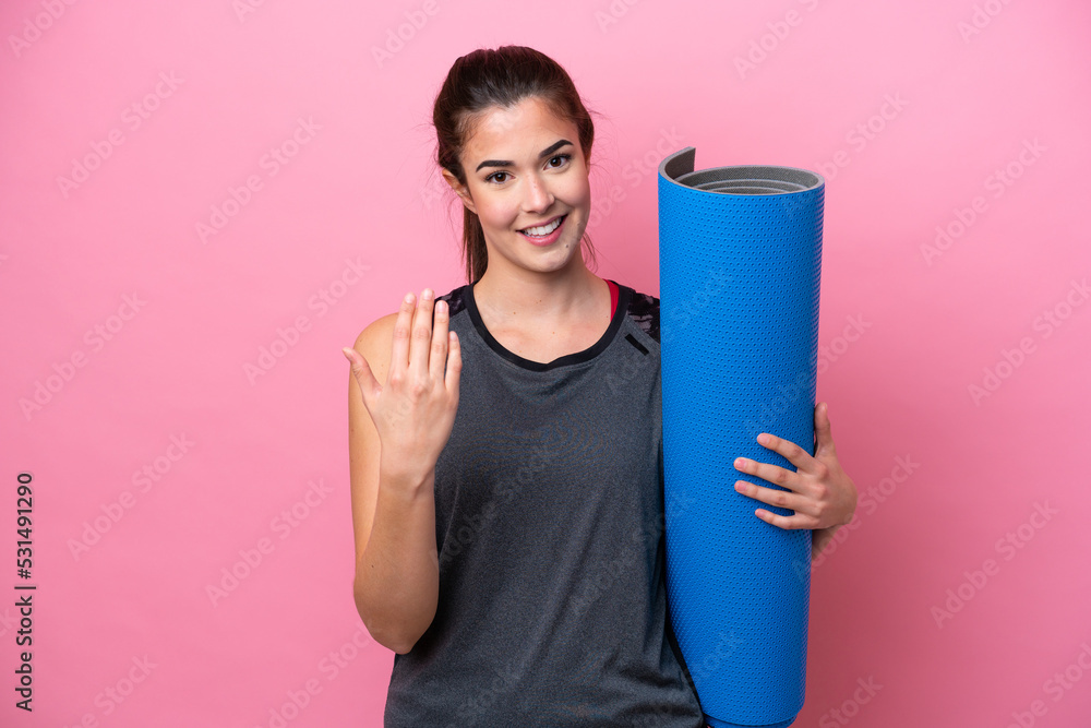 Young Brazilian sport woman going to yoga classes while holding a mat isolated on pink background inviting to come with hand. Happy that you came Young Brazilian sport woman going to yoga classes while holding a mat isolated on pink background inviting to come with hand. Happy that you came