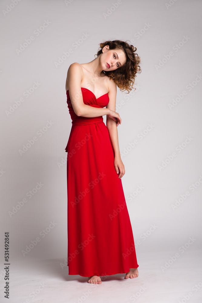 High fashion photo of a beautiful elegant young woman in a pretty long red dress, hairstyle on white, soft gray background. Studio Shot. 