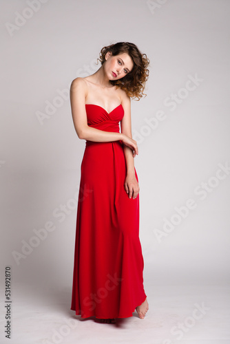 High fashion photo of a beautiful elegant young woman in a pretty long red dress, hairstyle on white, soft gray background. Studio Shot. 