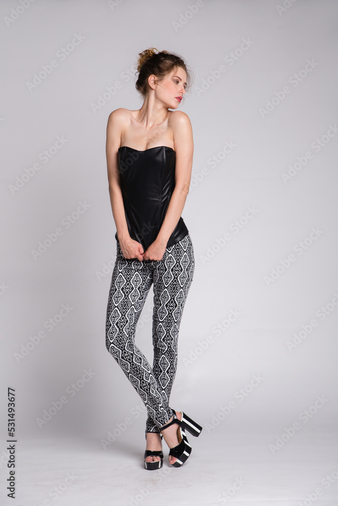 High fashion photo of a beautiful elegant young woman in a pretty black leather corset, gray pants on white background. Studio Shot. High fashion photo of a beautiful elegant young woman in a pretty black leather corset, gray pants on white background. Studio Shot.