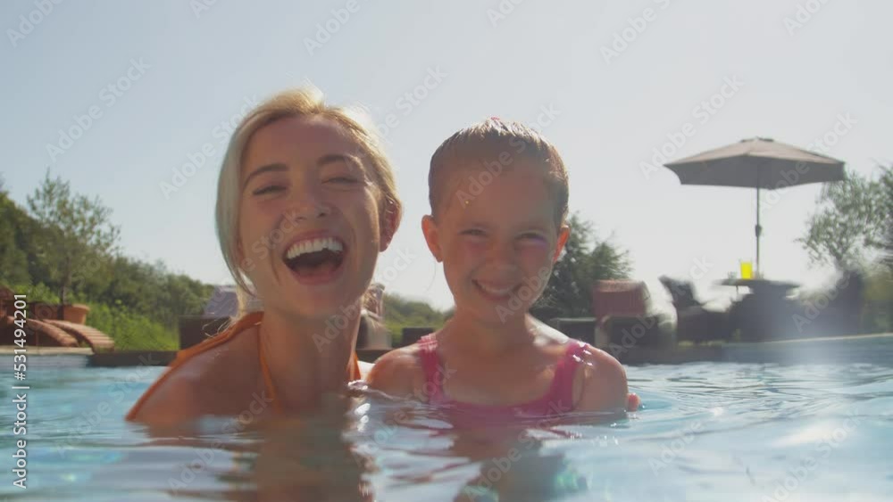 Portrait of smiling mother and daughter having fun on family summer holiday splashing in swimming pool - shot in slow motion Portrait of smiling mother and daughter having fun on family summer holiday splashing in swimming pool - shot in slow motion