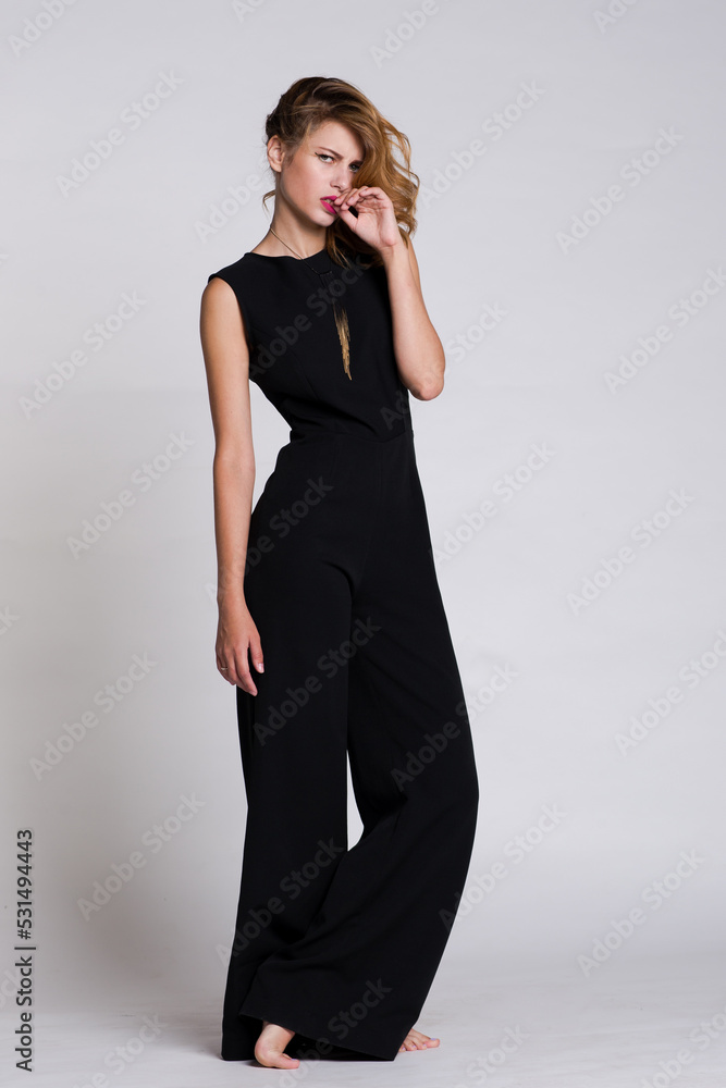 Fototapeta premium Fashion photo of a beautiful elegant model posing in the Studio. Black jumpsuit. White, soft gray background. Studio Shot. Portrait