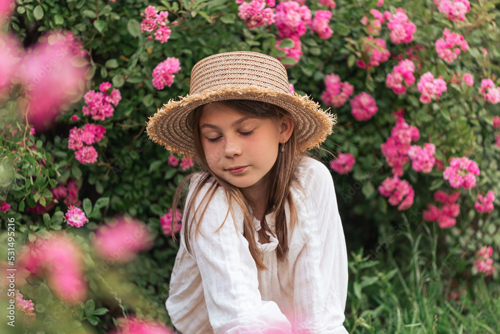 Cute little girl with blond hair in a straw hat. Pink flowers. Summer.