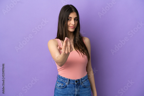 Young caucasian woman isolated on purple background inviting to come with hand. Happy that you came