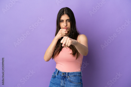 Young caucasian woman isolated on purple background with fighting gesture © luismolinero