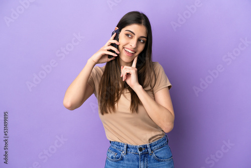 Young caucasian woman using mobile phone isolated on purple background thinking an idea while looking up