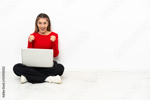 Young caucasian woman with a laptop sitting on the floor celebrating a victory in winner position