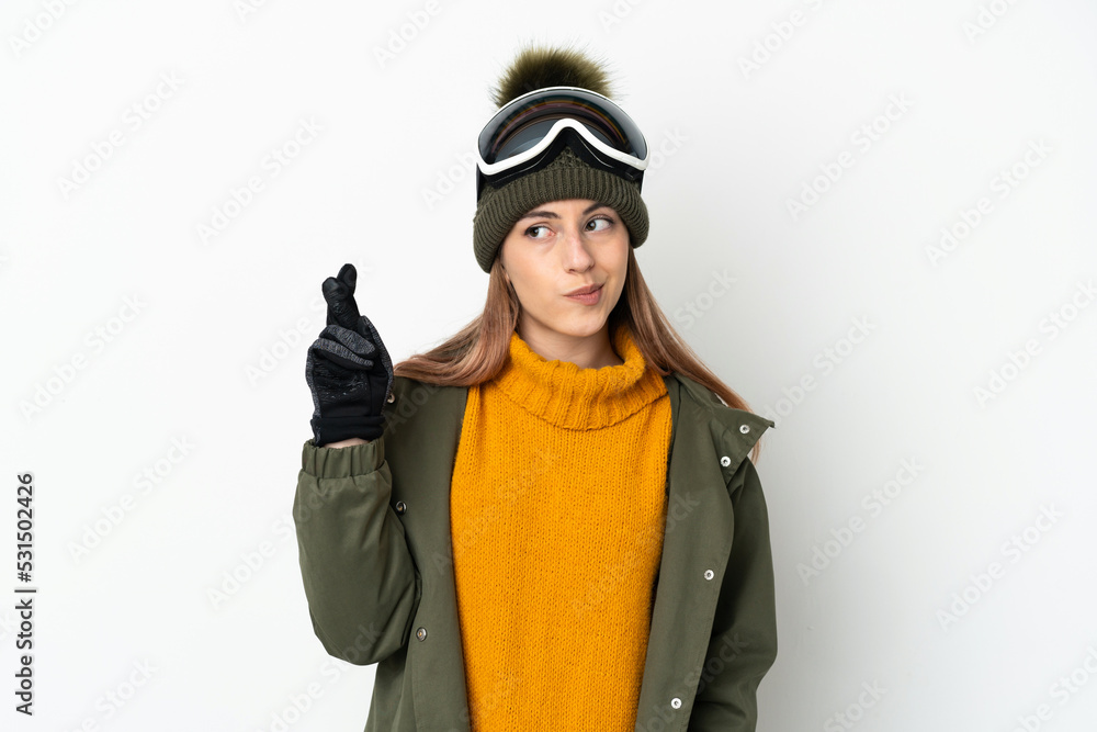 Skier caucasian woman with snowboarding glasses isolated on white background with fingers crossing and wishing the best