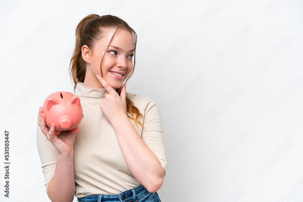 Young caucasian girl holding a piggybank isolated on white background thinking an idea and looking side Young caucasian girl holding a piggybank isolated on white background thinking an idea and looking side
