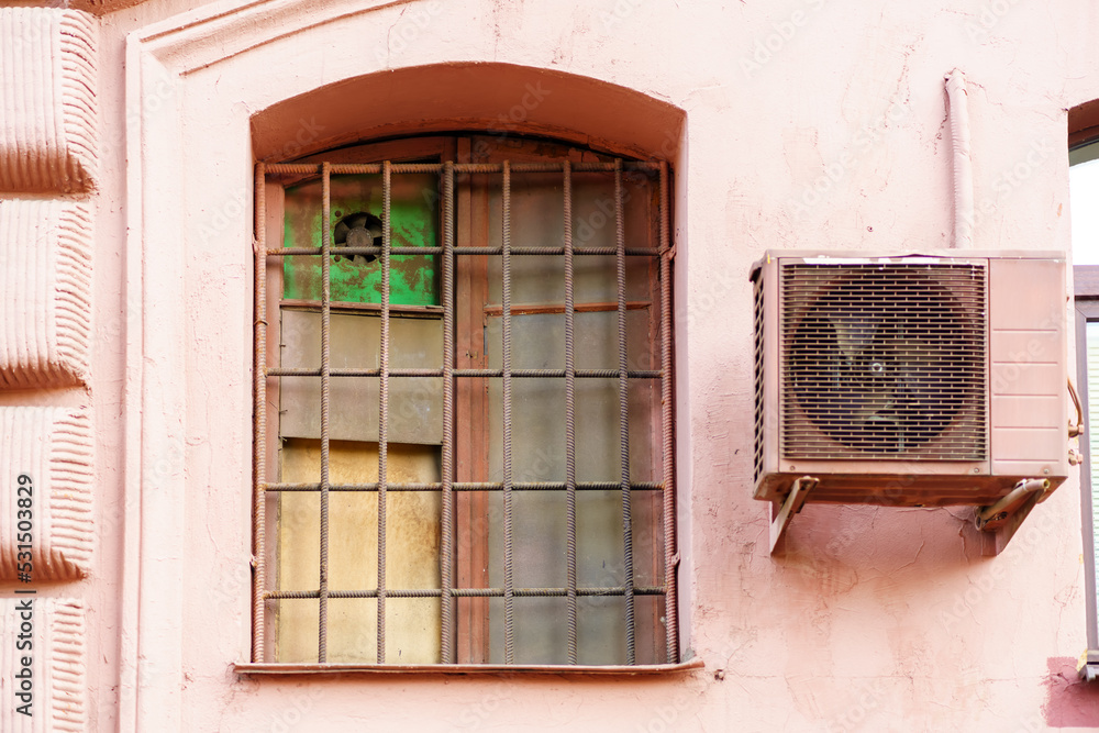 Window with a grille of fittings with dirty glass in the house of pink color